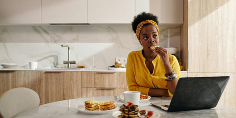 A Black woman eating food while sitting in front of a laptop