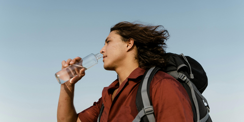 A Caucasian man wearing a maroon shirt drinking from a bottle of water